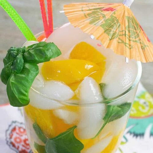 An orange cocktail umbrella stuck in a drink made with peaches and fresh basil.