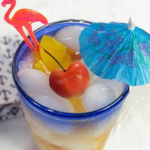 A flamingo pick rests in a cocktail garnished with a Rainier cherry.