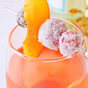 A close up of a Sugar Plum Fairy cocktail garnish with a cocktail pick with sugared grapes and cranberries with a plum slice.