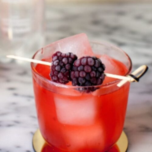 A berry cocktail on a gold coaster with a fresh berry garnish.