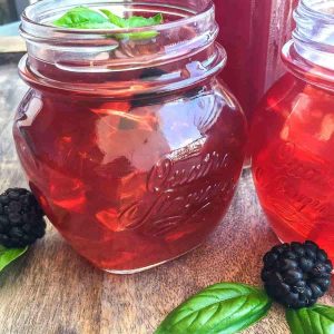 Two jars serving blackberry iced tea on a wood table with fresh basil.