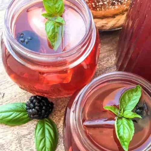 Overhead shot of two jars filled with blackberry sweet tea, garnished with fresh basil.