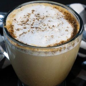 A latte sprinkled with cinnamon and cardamom spices on a black table.