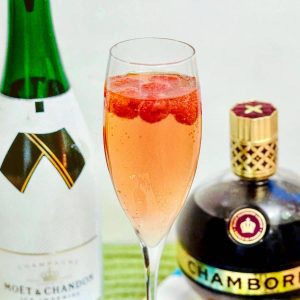 Raspberries float atop champagne in a flute next to a bottles of Moet Chandon champagne and Chambord liqueur