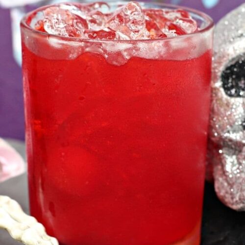 A red cocktails with cherries next to a silver glitter skull.