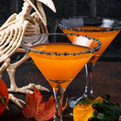 A pumpkin martini next to a skeleton of a bird decorated for Halloween.