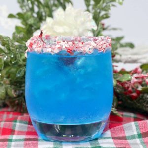 A blue cocktail in a glass edged with crushed peppermint on a plaid tablecloth.
