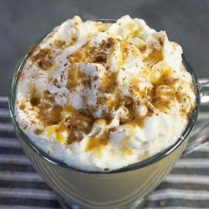 A clear mug of coffee topped with whipped cream, caramel syrup and cinnamon on a striped napkin.