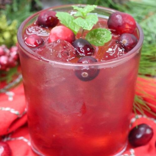 A cranberry margarita spritzer garnished with mint and fresh cranberries on a red napkin.