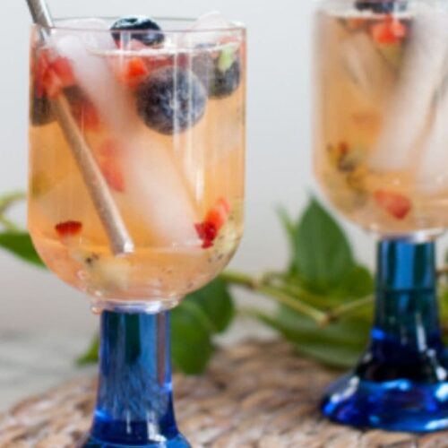 Fruity lemonade in wine glasses with blue stems on a braided placemat.