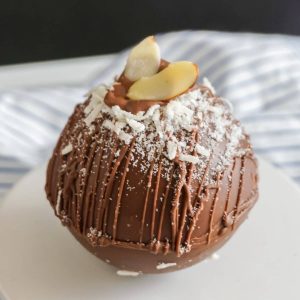 A coconut rum hot chocolate bomb on a cupcake stand topped with coconut and almonds.