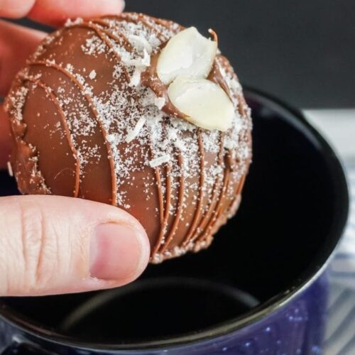 A hot chocolate bomb being placed in a blue mug.