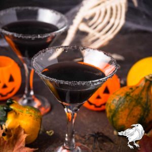 A black vodka martini pictured with gourds, autumn leaves, and jack-o-lanterns with a toy raven skeleton.