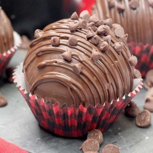 A hot chocolate bomb with mini chocolate chips on top in a buffalo plaid cupcake holder.