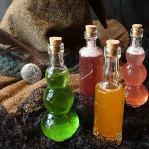 Four small glass bottles with colored beverages next to a witch hat.