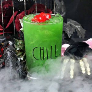 A Midori margarita with cherries next to a bony hand with dry ice smoke floating around the beverage glass.