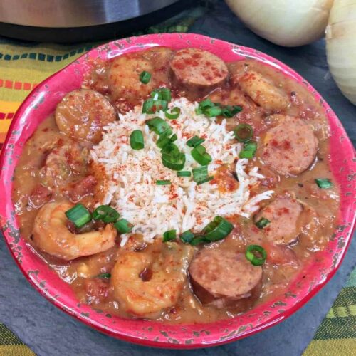 A red bowl with gumbo made from shrimp, sausage and chicken with rice and green onions.