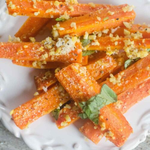 Roasted carrots with minced garlic and fresh basil on a white plate.