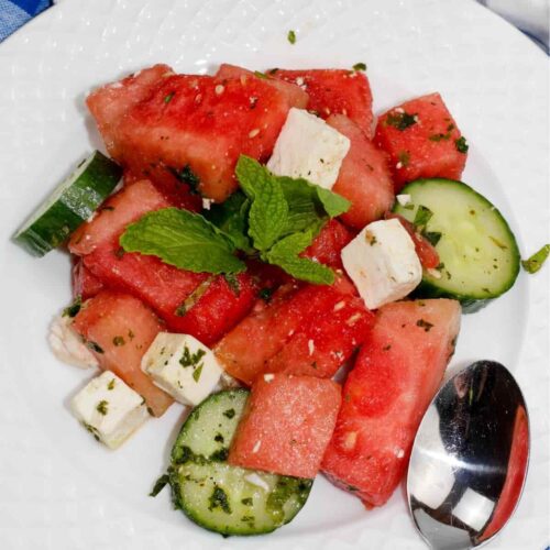 A serving of watermelon, cucumber, and feta salad on a plate with a spoon.