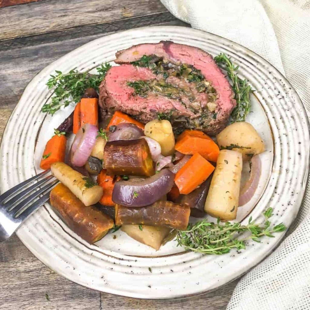 A plate of stuffed beef tenderloin with roasted vegetables and fresh herbs.