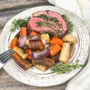 Beef tenderloin with root vegetables on a white plate with a fork.